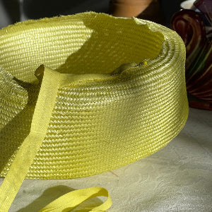 A citrus coloured straw headpiece in progress with pins on a milliner workbench.
